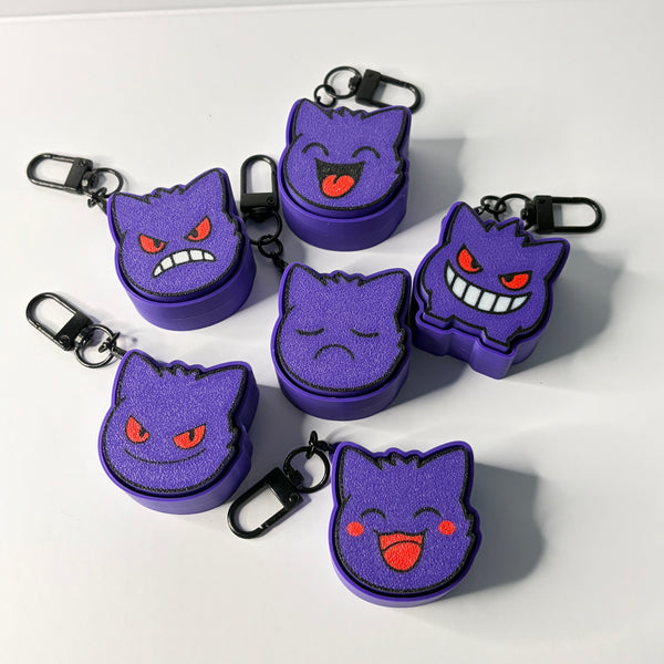 Six small purple cat-face keychain cases with black carabiners, arranged on a white background. The faces show different expressions, including angry, sad, and happy smiles, with red eyes and cheeks.